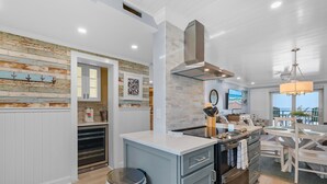 A modern kitchen with a central island, built-in appliances, and a dining area with a wooden table and chairs. - Sea Coast Gardens II 402 (New Smyrna Beach)