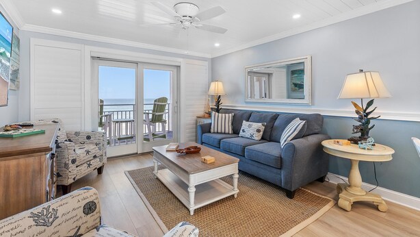 A living room with a blue sofa, white armchairs, a wooden coffee table, and a round side table with lamps. - Sea Coast Gardens II 402 (New Smyrna Beach)