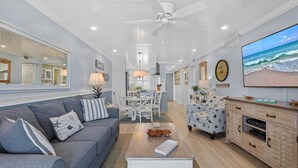 A living room with a grey sofa, a coffee table, a TV on the wall, and a ceiling fan. - Sea Coast Gardens II 402 (New Smyrna Beach)