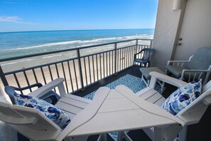A balcony with white chairs and a table, overlooking a beach with waves and a clear sky. - Sea Coast Gardens II 405 (New Smyrna Beach)