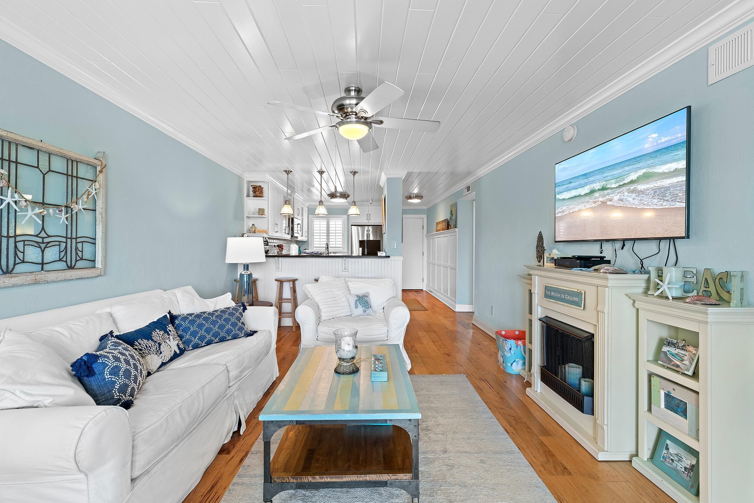 A living room with a white sofa, a coffee table, a fireplace, and a TV on the wall.