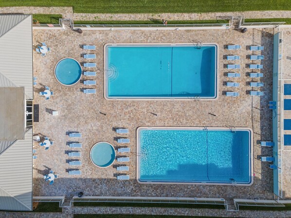An aerial view of a pool area with two rectangular pools, surrounded by lounge chairs and tables.