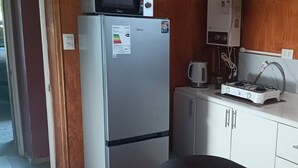 Een compacte keuken met een koelkast, magnetron, gasfornuis en een klein spoelbakje.