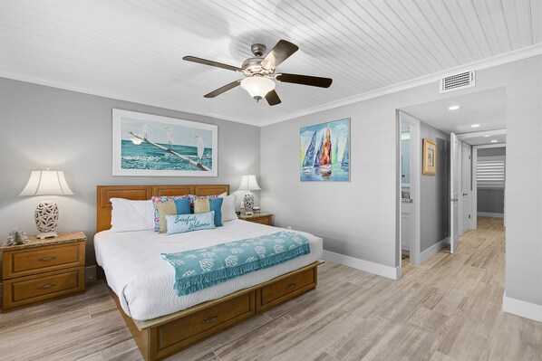 Un dormitorio con cama, mesitas de noche, ventilador de techo y obras de arte en las paredes.