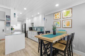 A modern kitchen with white cabinetry, a wooden island, and a dining area with a table and chairs. - Sea Coast Gardens III 109 (New Smyrna Beach)