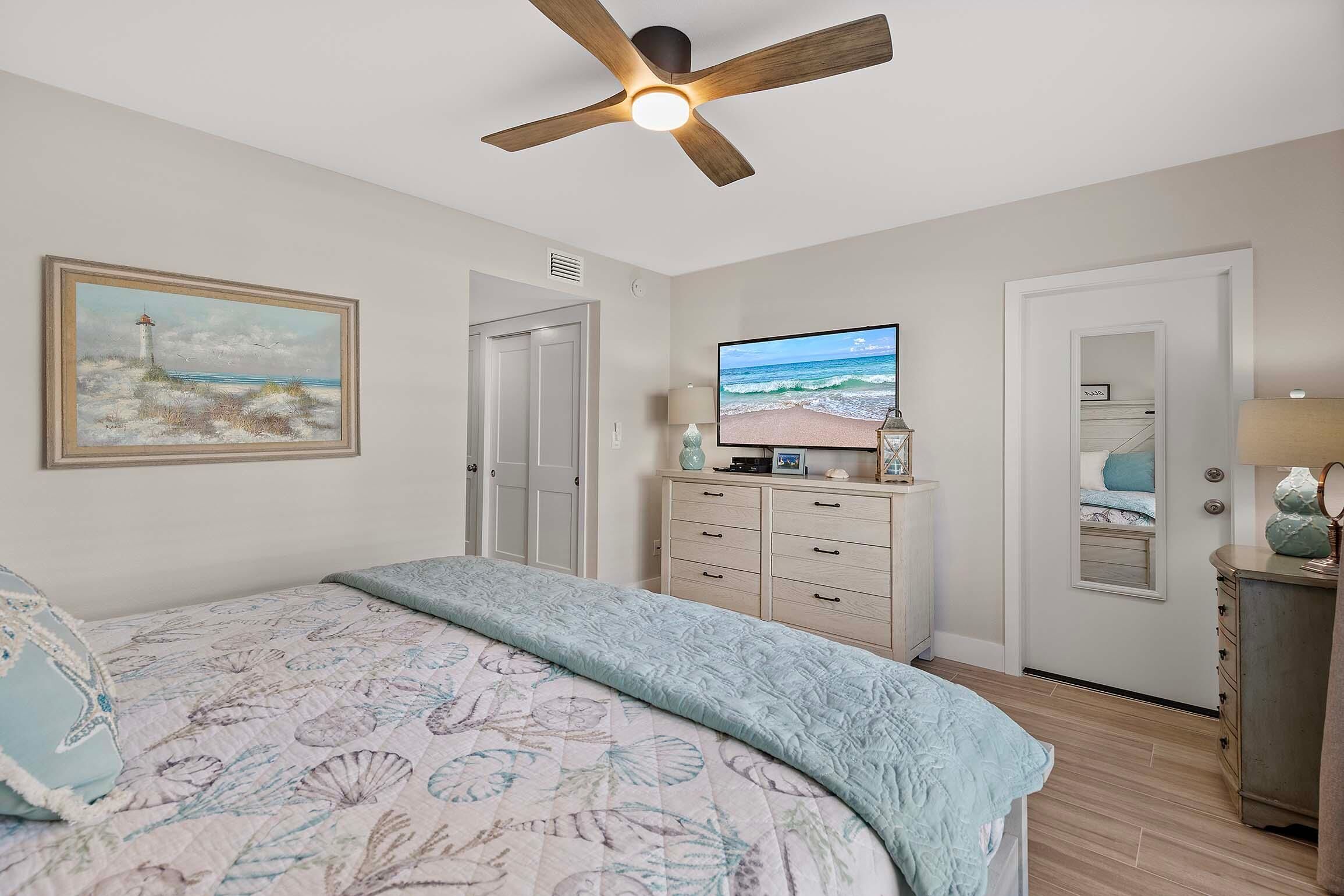 A bedroom with a bed, a ceiling fan, a TV, a dresser, and a painting on the wall.