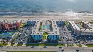 An aerial view of a coastal hotel with multiple buildings, a parking lot, and a beach. - Sea Coast Gardens III 111 (New Smyrna Beach)