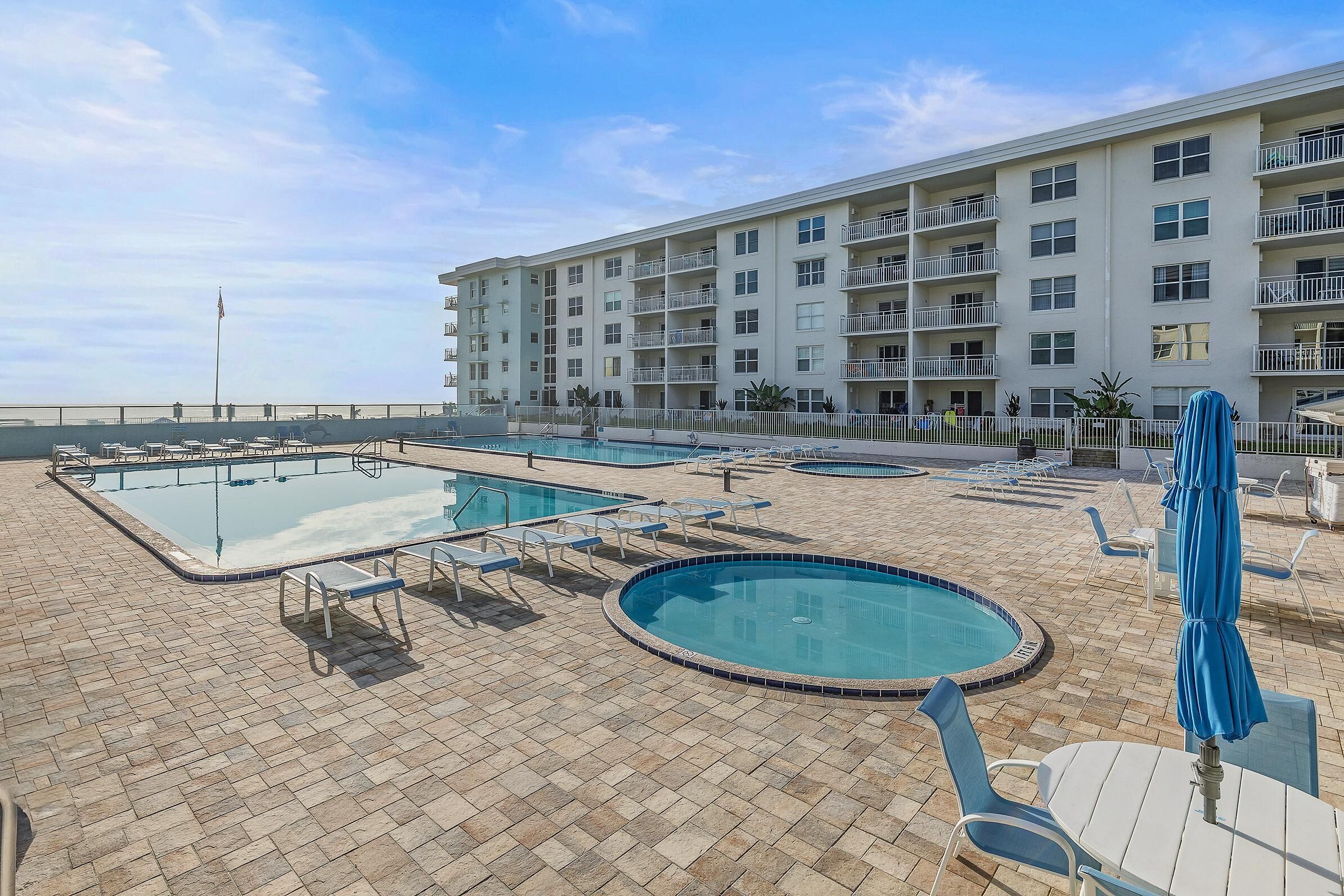 A hotel pool area with multiple pools, lounge chairs, and umbrellas.
