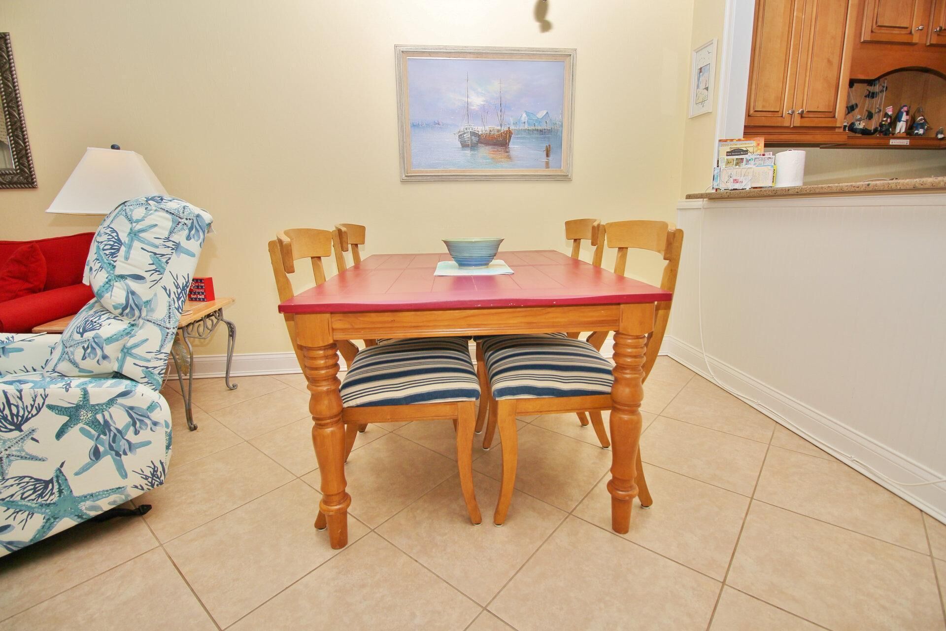 A dining area with a wooden table and chairs, a red cushion, a blue patterned sofa, and a painting on the wall.