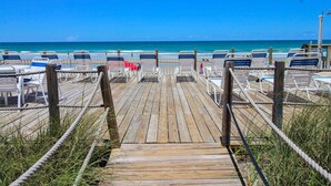 A wooden boardwalk leading to beach chairs and tables, overlooking the ocean.