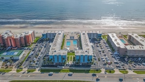 Ein Luftbild eines Küstenhotels mit mehreren Gebäuden, einem Parkplatz und einem Strand.