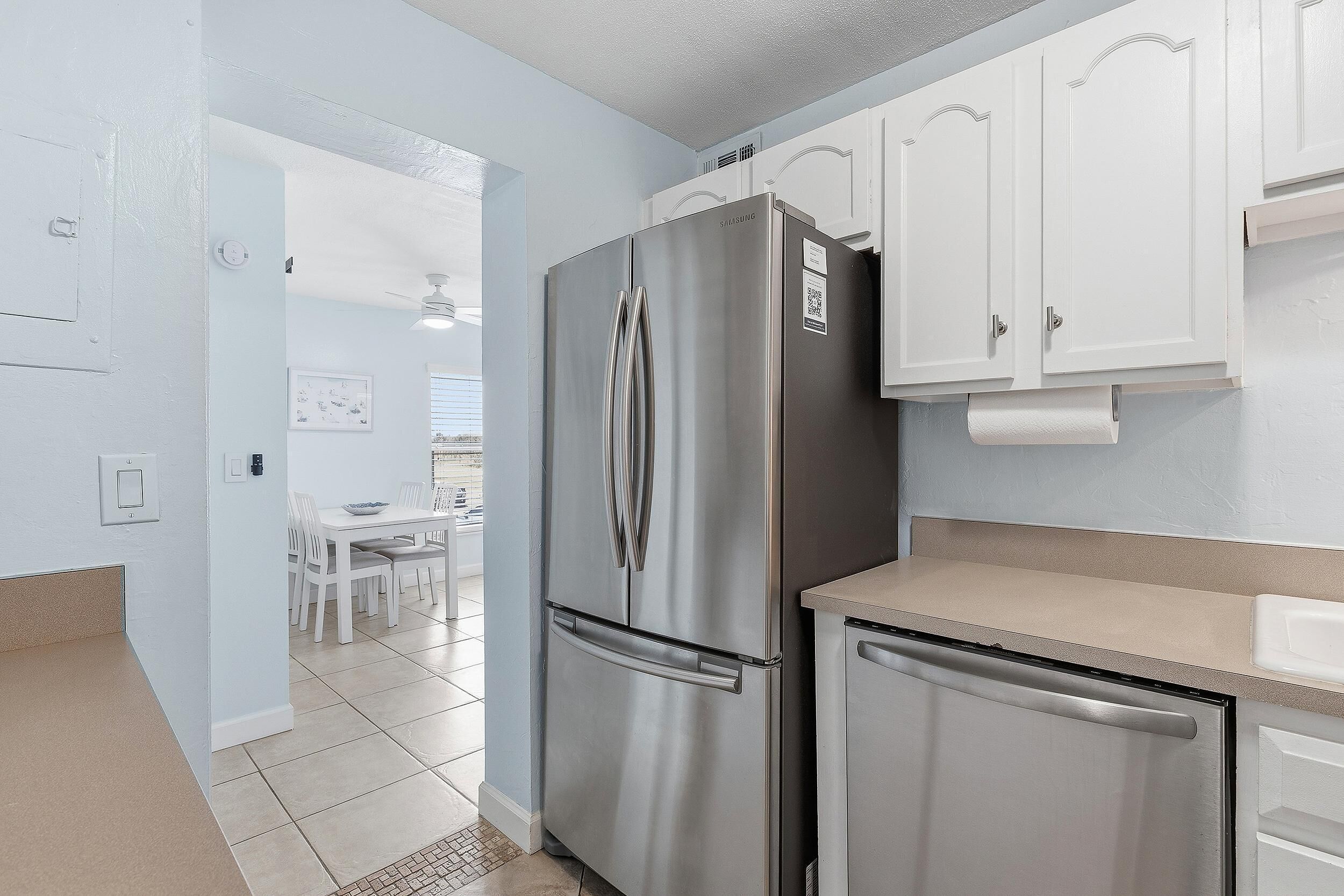 A kitchen with a stainless steel refrigerator, a dishwasher, white cabinets, and a dining area with a table and chairs.