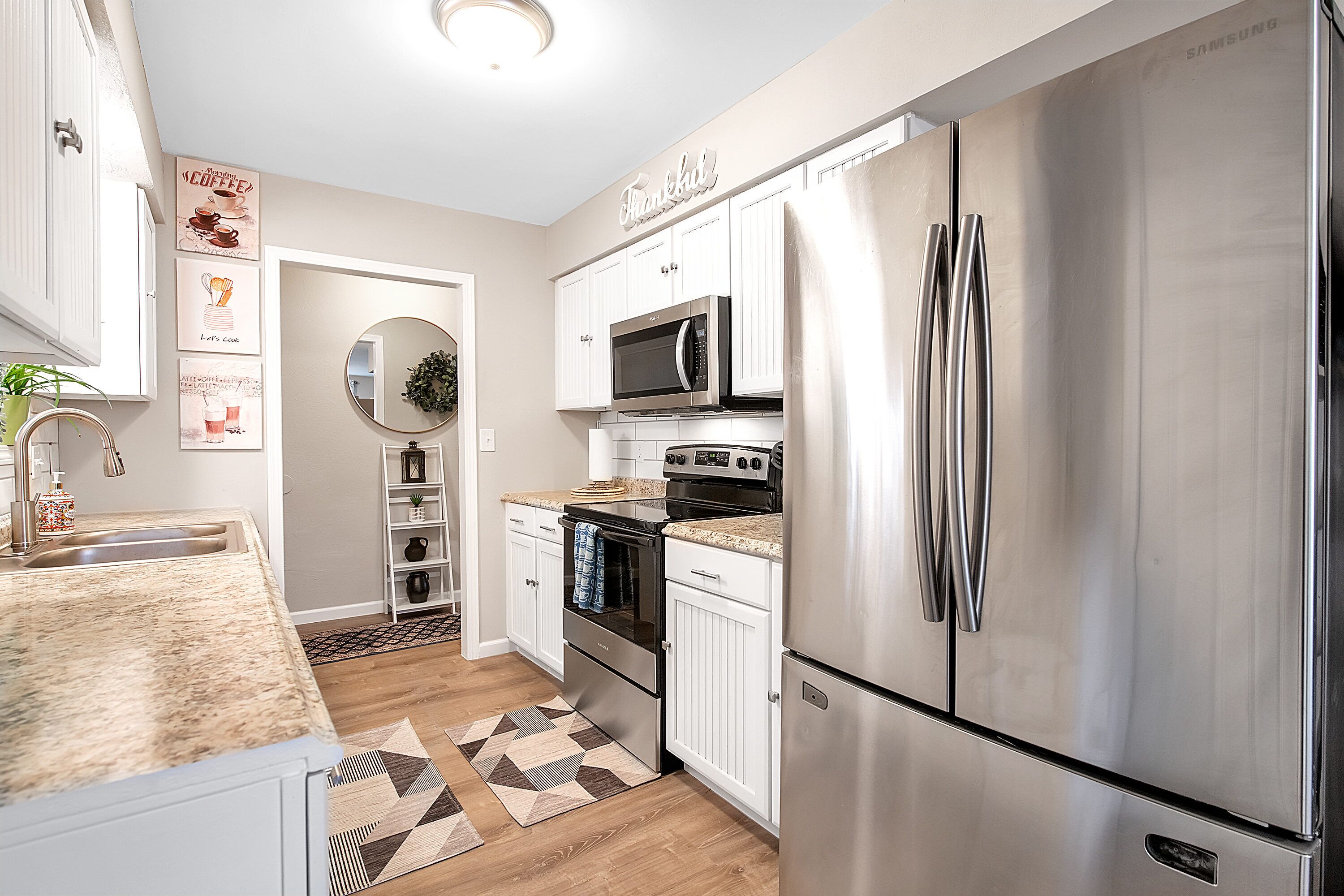 A modern kitchen with stainless steel appliances, white cabinetry, and a granite countertop.