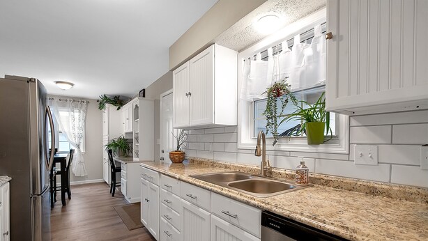 A modern kitchen with white cabinets, granite countertops, a dishwasher, and a window with plants. - Welcome to Valley View (Derby)