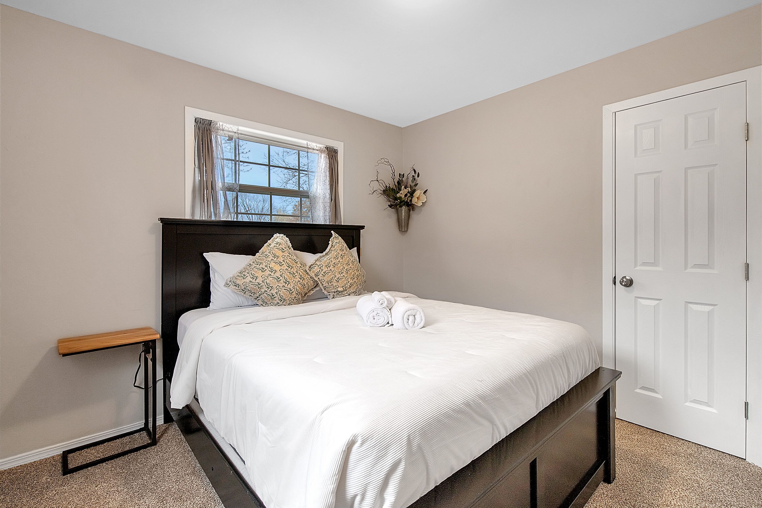 A neatly made bed with white bedding, a bedside table, and a window with curtains.