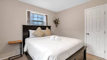 A neatly made bed with white bedding, a bedside table, and a window with curtains.