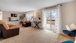 A living room with a brown sofa, a blue armchair, a small table with decorative items, and a TV mounted on the wall. - Welcome to Valley View (Derby)