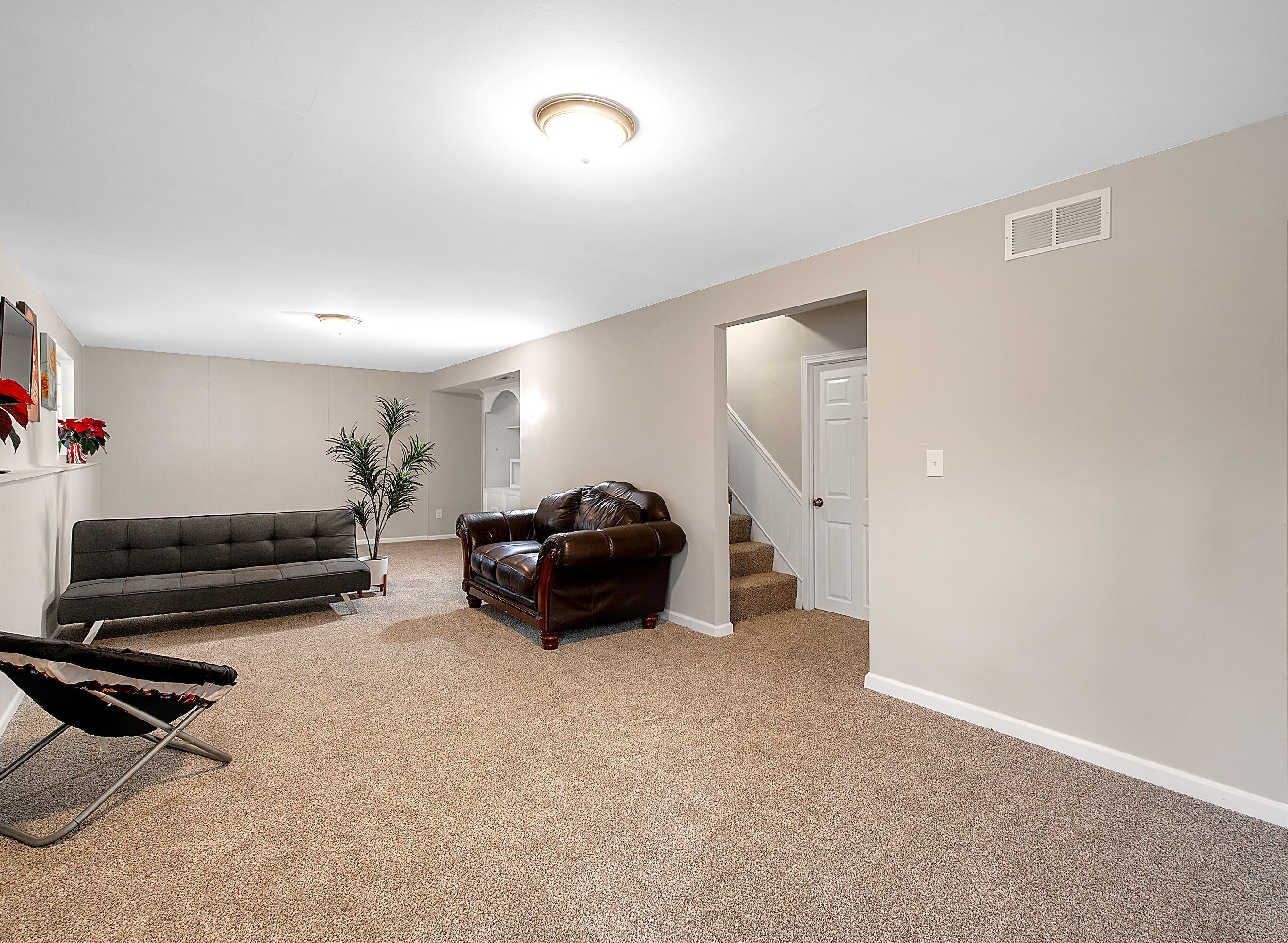 A spacious living room with a dark brown leather sofa, a grey sofa, and a potted plant. A folding chair is also visible.