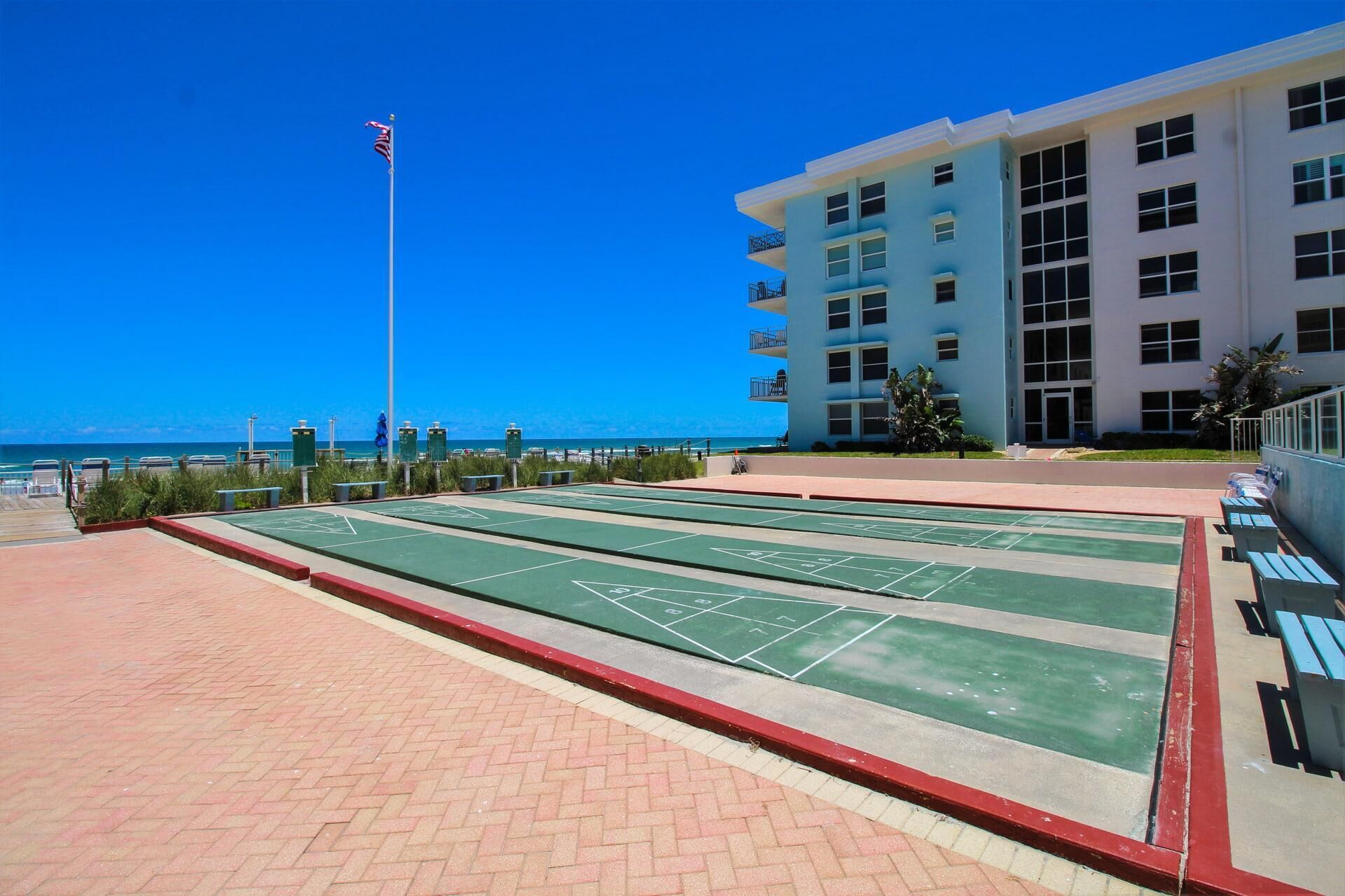 A courtyard with shuffleboard tables, a flagpole, and a building with balconies.