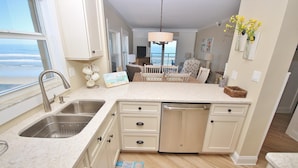 A kitchen with a large window, a dishwasher, and a dining area with a view of the ocean. - Sea Coast Gardens III 406 (New Smyrna Beach)