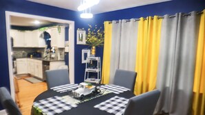 Un comedor con una mesa redonda, sillas y mantel negro. Se ve una cocina a través de un vano abierto.