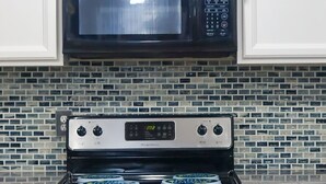 Una cocina con armarios blancos, una estufa de acero inoxidable y un microondas negro.