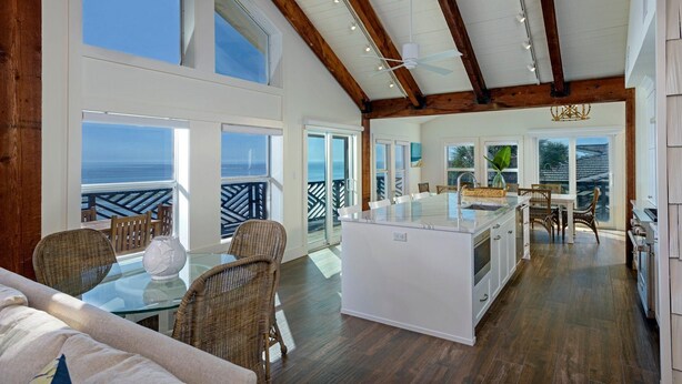 A spacious living area with a glass-top table, wicker chairs, a sofa, and a kitchen area with white cabinets and a large island. - Sea Castle (New Smyrna Beach)