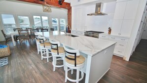 A modern kitchen with a large island, white cabinetry, and a dining area with wooden chairs. - Sea Castle (New Smyrna Beach)