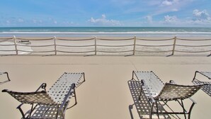 A beach with a fence, two metal lounge chairs, and a clear view of the ocean. - Sea Castle (New Smyrna Beach)