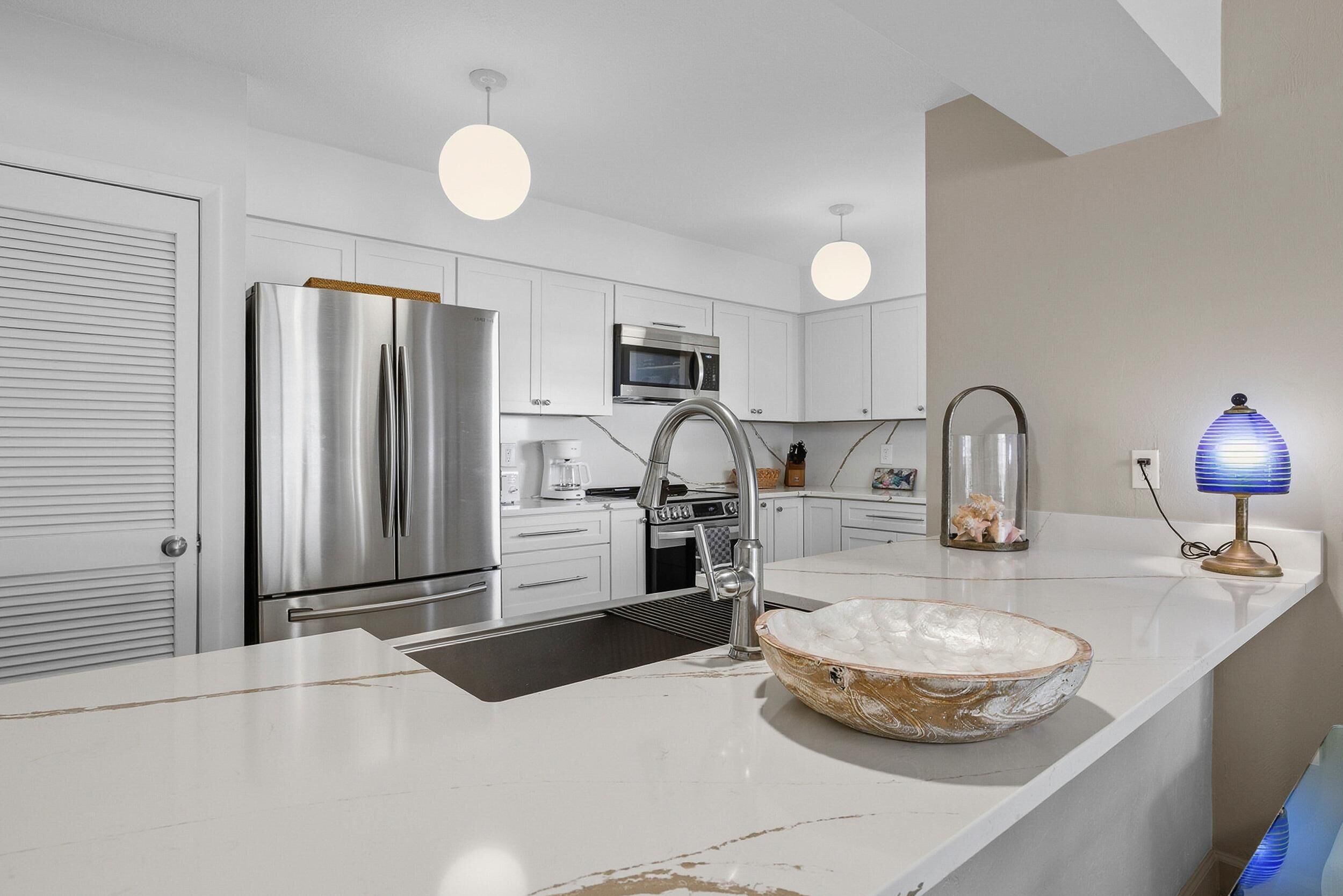 Una cocina moderna con electrodomésticos de acero inoxidable, una encimera blanca e iluminación colgante.