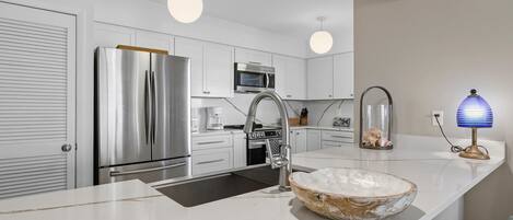 Una cocina moderna con electrodomésticos de acero inoxidable, una encimera blanca e iluminación colgante.