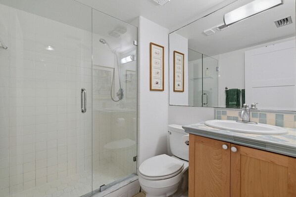 Un baño moderno con cabina de ducha de vidrio, un inodoro y un lavabo con espejo.