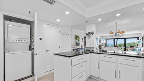 Cocina moderna con armarios blancos, encimera negra y vistas al océano a través de amplios ventanales.