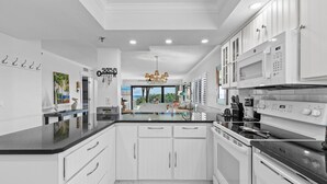 Una cocina moderna con armarios blancos, encimera negra y electrodomésticos de acero inoxidable.