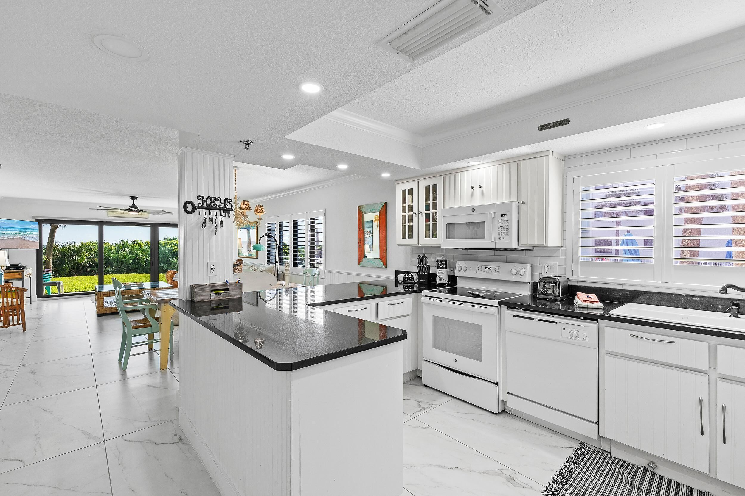A modern kitchen with white cabinets, a black countertop, and a view of the outdoors.