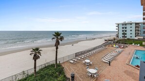Une vue sur la plage avec une piscine, des palmiers et un bâtiment en arrière-plan.