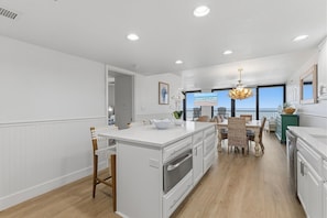 A modern kitchen with a central island, white cabinetry, and a dining area with wicker chairs. - Sunrise 309 (New Smyrna Beach)