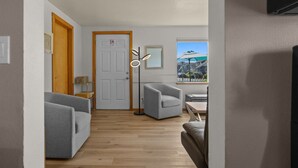 A hallway with a wooden floor, grey sofas, a small table, and a door with a sign. - Dream retreat, a block from sand and ocean (Cannon Beach)