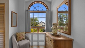 A room with a curved gray armchair, a wooden dresser, and a large arched window with a view of houses.