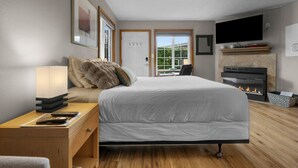 A modern bedroom with a large bed, bedside table, lamp, and a fireplace.