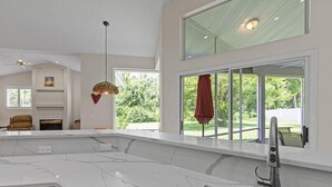 Eine moderne Küche mit einer großen Kochinsel, einem eingebauten Ofen und einem großen Fenster mit Blick auf Grünflächen.
