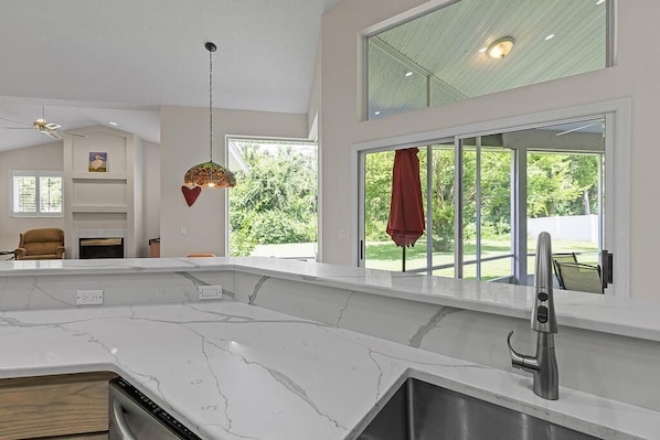 A modern kitchen with a large island, a built-in oven, and a large window with a view of greenery. - Sunrise Oaks (Port Orange)