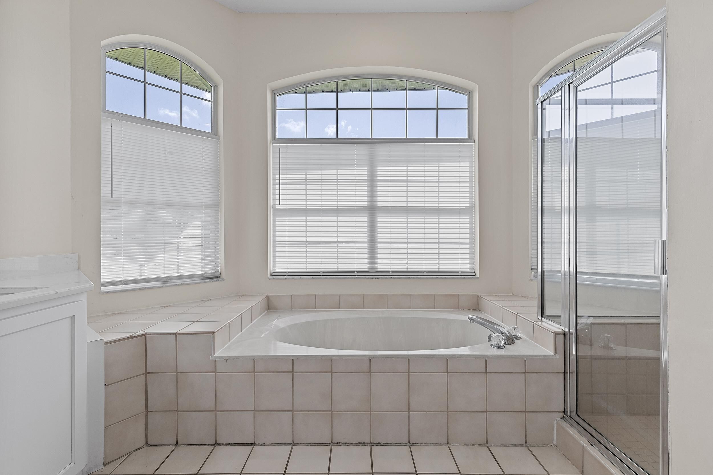 A bathroom with a large bathtub, a shower, and three windows with blinds.