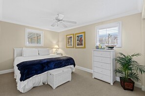 A bedroom with a bed, a ceiling fan, a dresser, a window with blinds, and a potted plant.