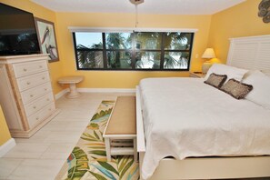 Une chambre à coucher avec un lit, une commode, une fenêtre, une lampe et un tableau au mur.