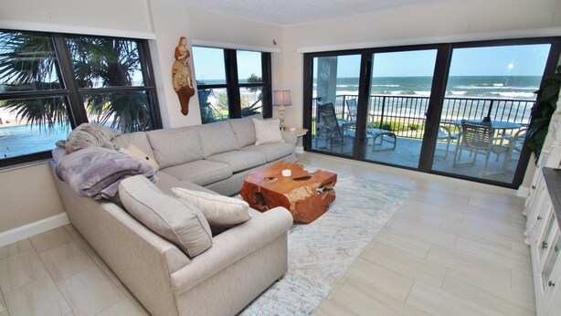 Een woonkamer met een beige bank, een houten salontafel en grote ramen met uitzicht op de oceaan.