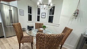 Una cocina moderna con una mesa redonda de cristal, sillas tejidas, electrodomésticos de acero inoxidable y una araña.