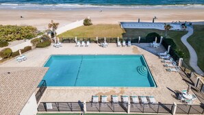 Ein Poolbereich mit Liegestühlen und Blick auf Strand und Meer.