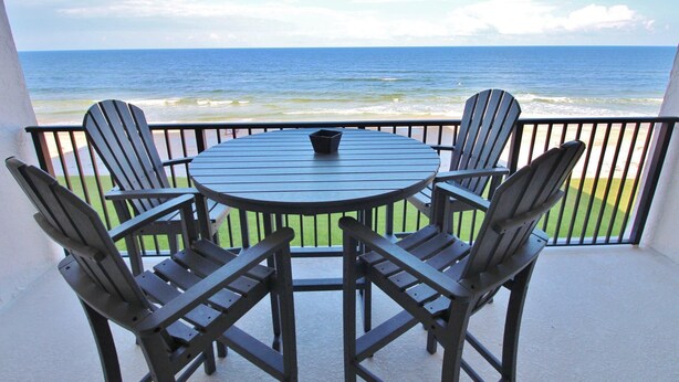 Ein runder Tisch mit vier Stühlen auf einem Balkon mit Blick aufs Meer.