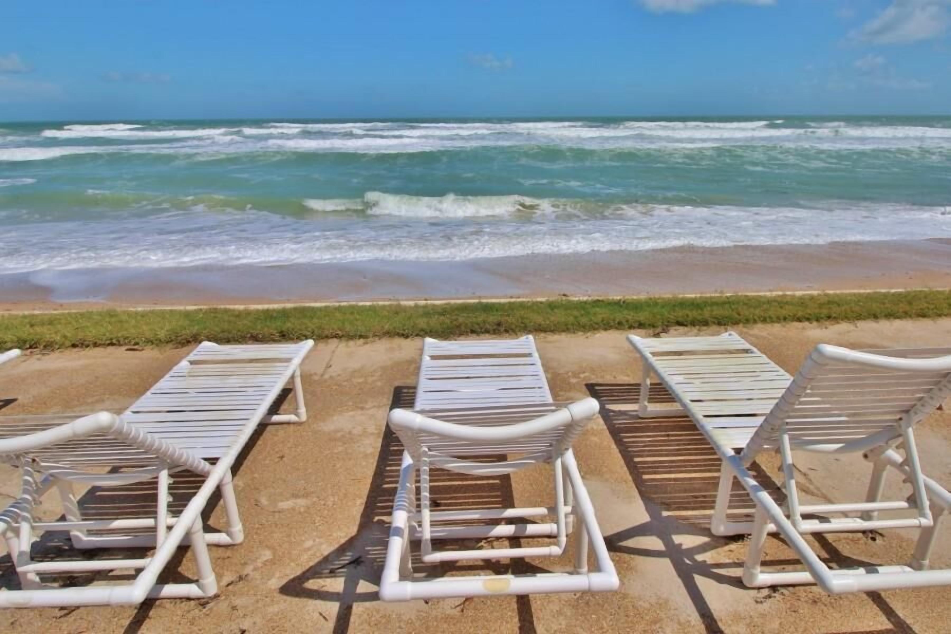 A beach with white lounge chairs arranged in rows facing the ocean.